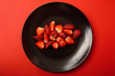 Kırmızı arka planda siyah tabakta kırmızı böğürtlen. Tarifler için sulu bir yaz geçmişi. Tabakta böğürtlen.