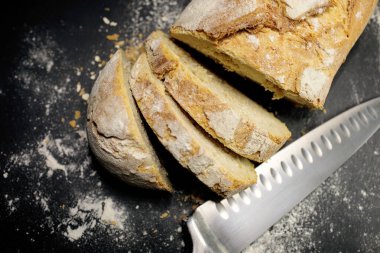 Siyah zemin üzerinde un ile ev yapımı taze ekmek. Bıçakla kesilmiş. Üst görünüm.