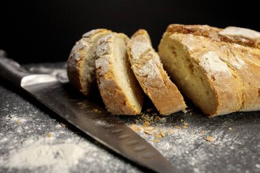 Siyah zemin üzerinde un ile ev yapımı taze ekmek. Bıçakla kesilmiş. Yan görünüm.