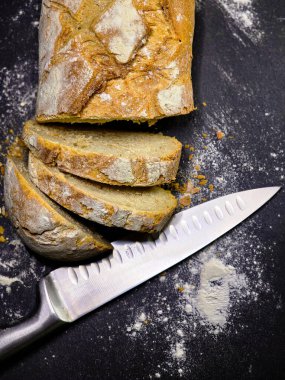 Bıçaklı üst görüşe yakın siyah arkaplanda ev yapımı beyaz çavdar ekmeği dilimlenmiş.