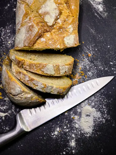 Bıçaklı üst görüşe yakın siyah arkaplanda ev yapımı beyaz çavdar ekmeği dilimlenmiş.