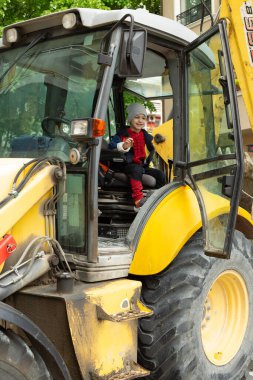Küçük çocuk büyük sarı bir traktör kullanıyor.