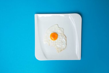 Mavi arka planda beyaz tabakta bir sahanda yumurta. Yiyeceğin kavramsal fotoğrafı. Sulu, parlak bir geçmişi var. Kahvaltıda. Sağlıklı.