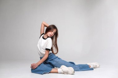 Güzel bir kız. Uzun saçlı, kot pantolonlu ve beyaz bluzlu. Beyaz arka planda fotoğraf stüdyosunda. Farklı duygular. Duygusal bir çekim. Modellik. Fotoğraf mankeni. Fotoşop