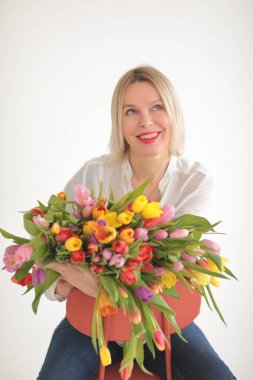 Beyaz arka planda güzel, mutlu, sarışın bir kadın. Fotoğraf stüdyosunda büyük bir buket lale ile.
