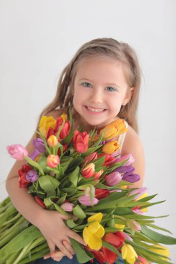 Büyük bir buket lale ile bir fotoğraf stüdyosunda beyaz arka planda beyaz saçlı güzel mutlu küçük bir kız. Anneler Günü.