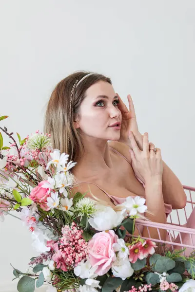 Çiçeklerle süslenmiş alışveriş arabası olan beyaz bir elbiseyle sarı saçlı güzel bir genç kız. Fotoğraf mankeni. Model.