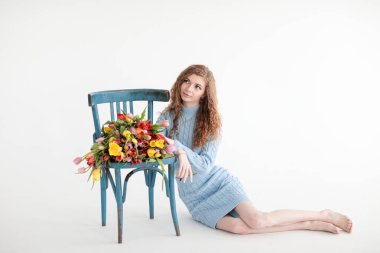 Kırmızı kıvırcık saçlı güzel bir genç kız ve beyaz bir arka planda, yumuşak mavi bir elbiseyle kocaman bir buket çok renkli laleyle bir fotoğraf stüdyosunda kocaman gözleri var. Fotoğraf mankeni. Model.