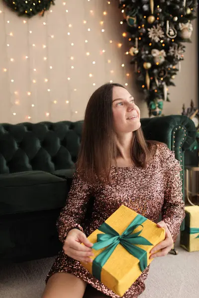 Noel ağacının yanında siyah mini elbiseli güzel bir kız ve fotoğraf stüdyosunda koyu yeşil bir kanepe. Fotoğraf mankeni. Modellik. Yeni yıl. Noel.