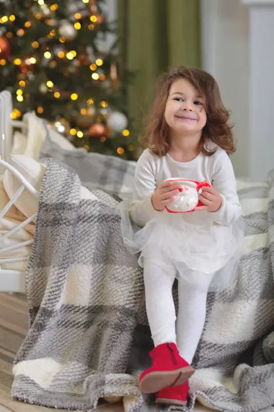 Küçük kız elinde bir yılbaşı ağacıyla yerde oturuyor. Mutlu çocuk oturma odasında..