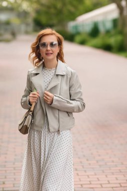 Beyaz ceketli ve şapkalı güzel bir kadın şehir parkında yürüyor..