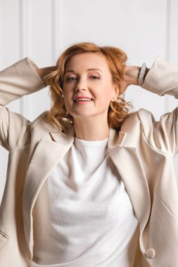 Beyaz ceketli kıvırcık saçlı çekici genç bir kadın. Gri arka planda izole edilmiş.