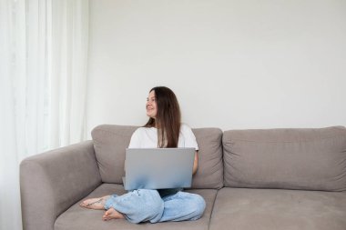 Genç Asyalı kadın evdeki koltukta, oturma odasında dizüstü bilgisayar kullanıyor. Yaşam tarzı kavramı.