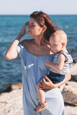 Güzel bir anne ile oğlu yazın sahilde yürüyorlar. Kumsalda.