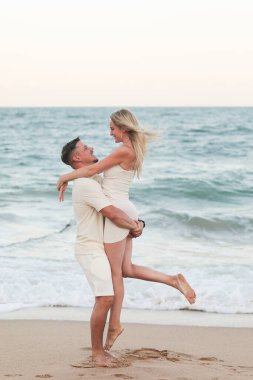 Beyaz elbiseli mutlu çift kumlu deniz kıyısında sarılıyor..