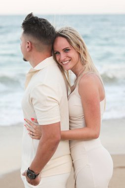 Gün batımında kumlu bir sahilde genç ve güzel bir çift. Adam gülümsüyor ve kız arkadaşına sarılıyor. Mutlu ve mutlu.