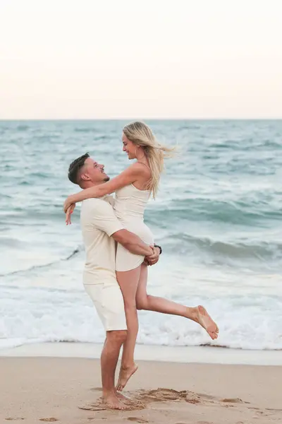 Beyaz elbiseli mutlu çift kumlu deniz kıyısında sarılıyor..