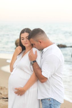 Genç, aşık hamile bir çift. Yazın sahilde, beyaz elbiseler içinde, denizde. Hamilelik. Karı koca. Annem ve babam. Annelik