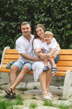 Mutlu genç bir aile, beyaz giysiler içinde, yazın parkta yürüyor. Annelik. Anne ve oğlu. Baba ve oğul. Anne, baba ve oğul. - Aile. Anneler Günü. Babalar Günü. Hamilelik. Hamile kız.