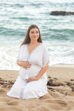 Yazın kumsalda beyaz elbiseli güzel bir kız. Hamilelik. Annelik