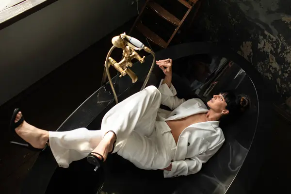 Beyaz takım elbiseli güzel genç kız fotoğraf stüdyosunda siyah küvette yatıyor.