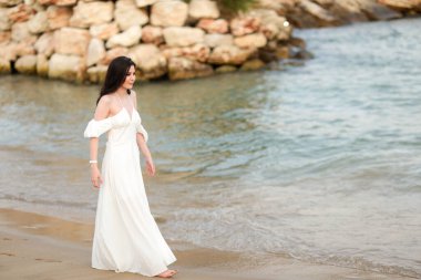 Yazın kumsalda, uzun siyah saçlı, beyaz, uzun elbiseli güzel bir kız.