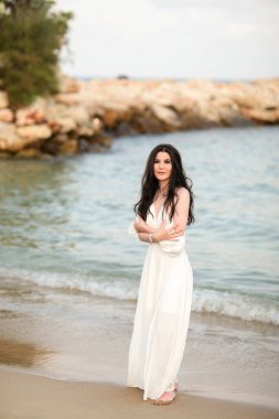 Yazın kumsalda, uzun siyah saçlı, beyaz, uzun elbiseli güzel bir kız.