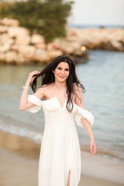 Yazın kumsalda, uzun siyah saçlı, beyaz, uzun elbiseli güzel bir kız.