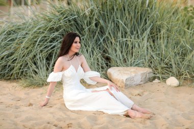 Yazın kumsalda, uzun siyah saçlı, beyaz, uzun elbiseli güzel bir kız.