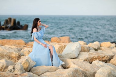 Uzun siyah saçlı, mavi uzun elbiseli güzel bir genç kız. Yazın sahilde.