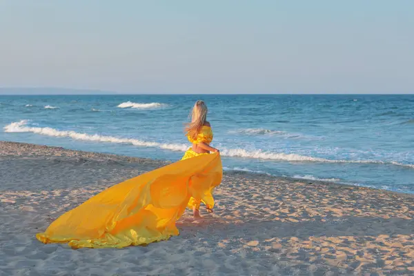 Uzun sarı saçlı, sarı uzun elbiseli, güzel bir genç kız. Yazın sahilde trenle geziyor.