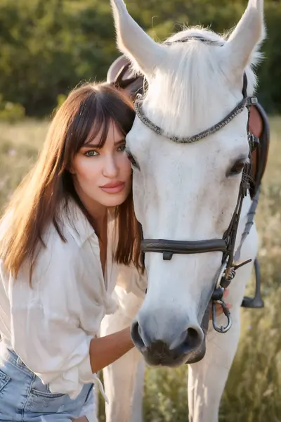 Çayırda beyaz bir atla siyah saçlı güzel bir genç kız.