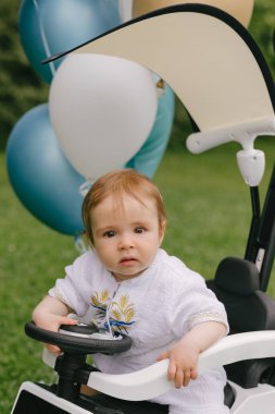 Küçük bebek, balonları çimlerin üzerine park etmiş beyaz bir arabada oturuyor. Ufaklık. Yaz.