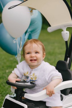 Küçük bebek, balonları çimlerin üzerine park etmiş beyaz bir arabada oturuyor. Ufaklık. Yaz.