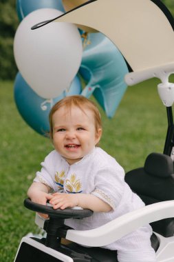 Küçük bebek, balonları çimlerin üzerine park etmiş beyaz bir arabada oturuyor. Ufaklık. Yaz.