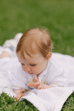 Yazın beyaz bir paspasın üzerinde çimlerin üzerinde oturan bir bebek.