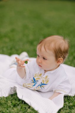 Yazın beyaz bir paspasın üzerinde çimlerin üzerinde oturan bir bebek.