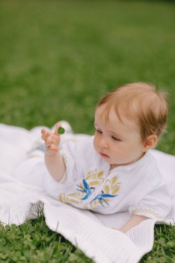 Yazın beyaz bir paspasın üzerinde çimlerin üzerinde oturan bir bebek.