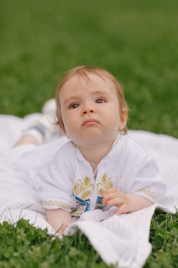 Yazın beyaz bir paspasın üzerinde çimlerin üzerinde oturan bir bebek.