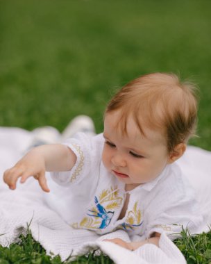 Yazın beyaz bir paspasın üzerinde çimlerin üzerinde oturan bir bebek.