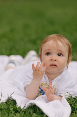 Yazın beyaz bir paspasın üzerinde çimlerin üzerinde oturan bir bebek.