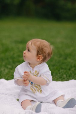 Yazın beyaz bir paspasın üzerinde çimlerin üzerinde oturan bir bebek.