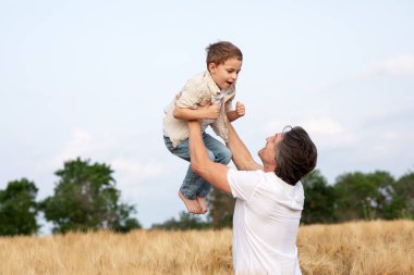 Mutlu bir baba ve oğlu yazın bir buğday tarlasında kollarında. Babalar Günü..