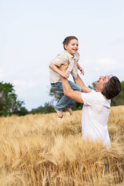 Mutlu bir baba ve oğlu yazın bir buğday tarlasında kollarında. Babalar Günü.