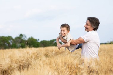 Mutlu bir baba ve oğlu yazın bir buğday tarlasında kollarında. Babalar Günü.