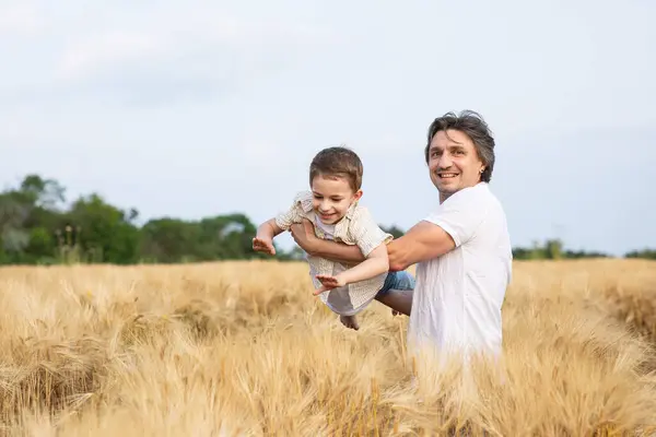 Mutlu bir baba ve oğlu yazın bir buğday tarlasında kollarında. Babalar Günü..
