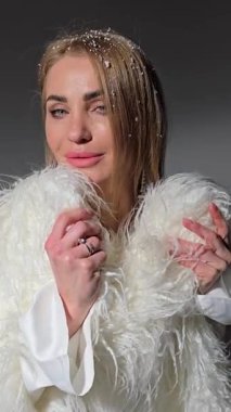 Fotoğraf stüdyosunda beyaz tüylü bir ceket giyen güzel sarışın kız. Modellik. Fotoğraf mankeni. Pozisyon