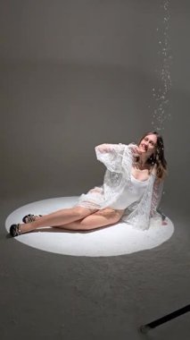 Bir fotoğraf stüdyosundaki beyaz bir pignoirin içinde genç ve güzel bir esmer. Modellik. Fotoğraf mankeni. Pozisyon