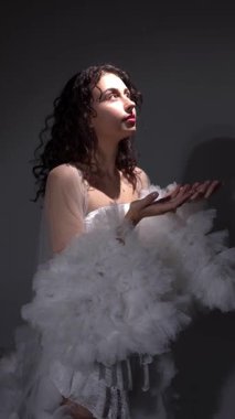 Bir fotoğraf stüdyosunda beyaz elbiseli ve pelerinli güzel bir genç kız. Fotoşop. Poz veriyorum. Fotoğraf modeli.