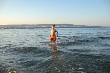 Turuncu şortlu mutlu çocuk yazın sahilde.